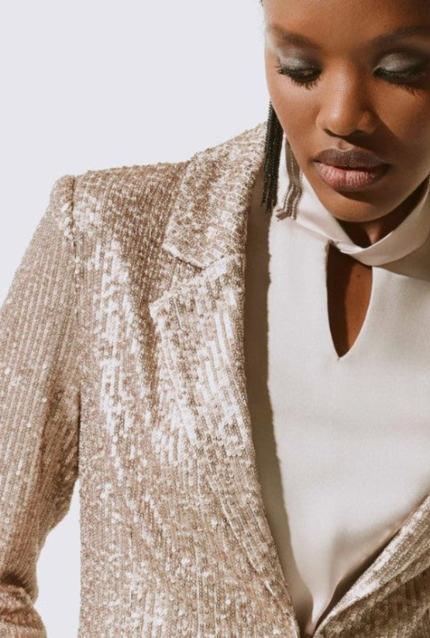 Woman wearing a sparkly beige blazer over a white top against a light background