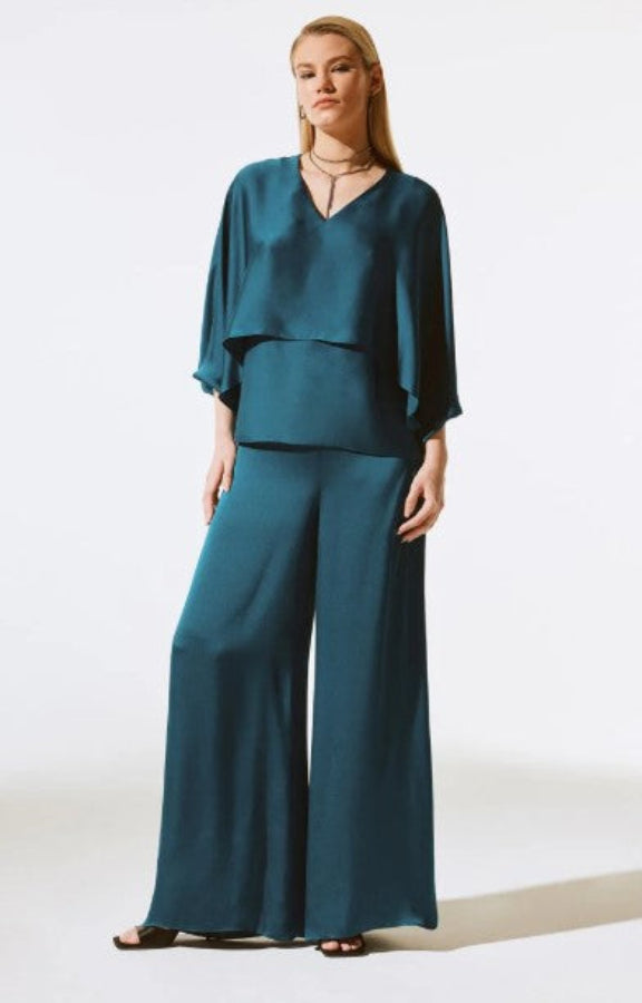 Woman wearing a teal outfit with a top and wide-leg pants on a white background