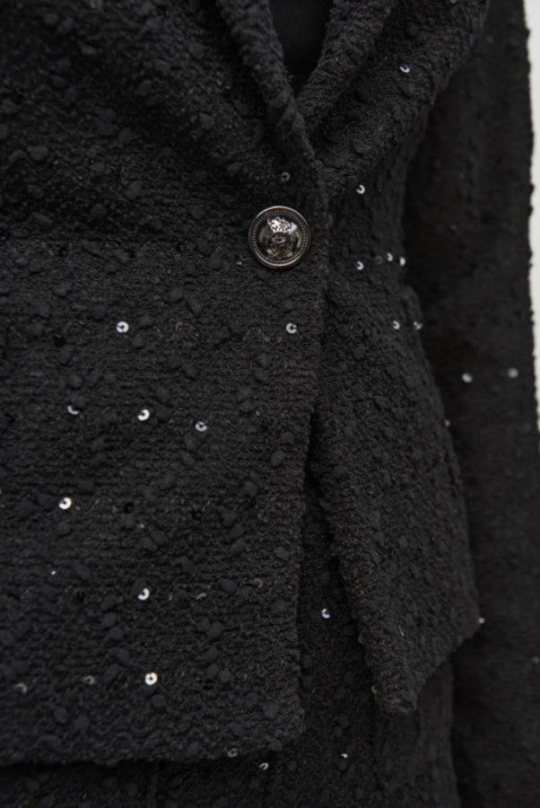 Close-up of a black textured coat with sequin details on a plain background