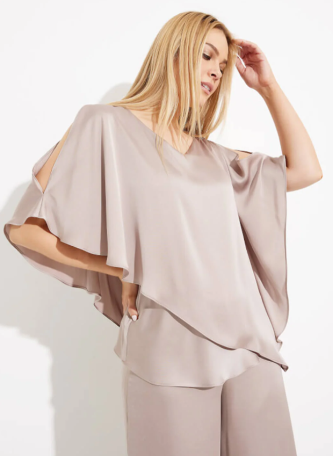 Woman wearing a beige outfit with a flowing top and pants against a white background