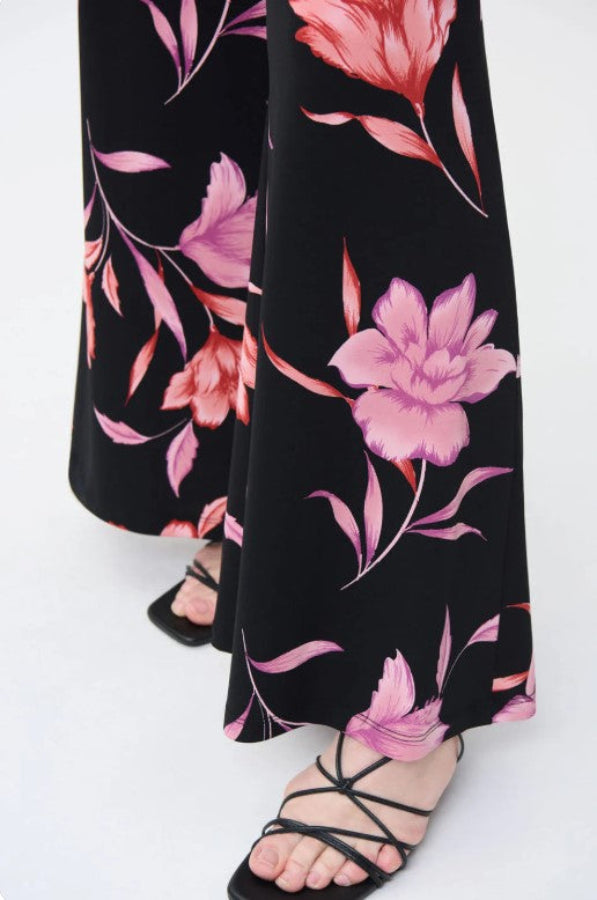 Black pants with pink floral pattern worn by a person on a white background