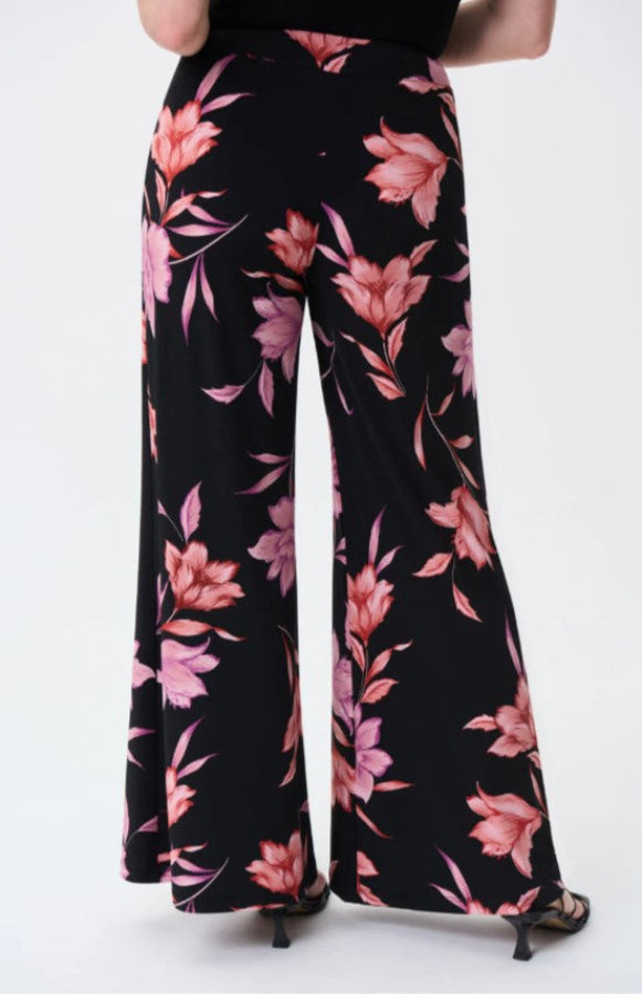 Black pants with pink floral pattern worn by a person on a white background