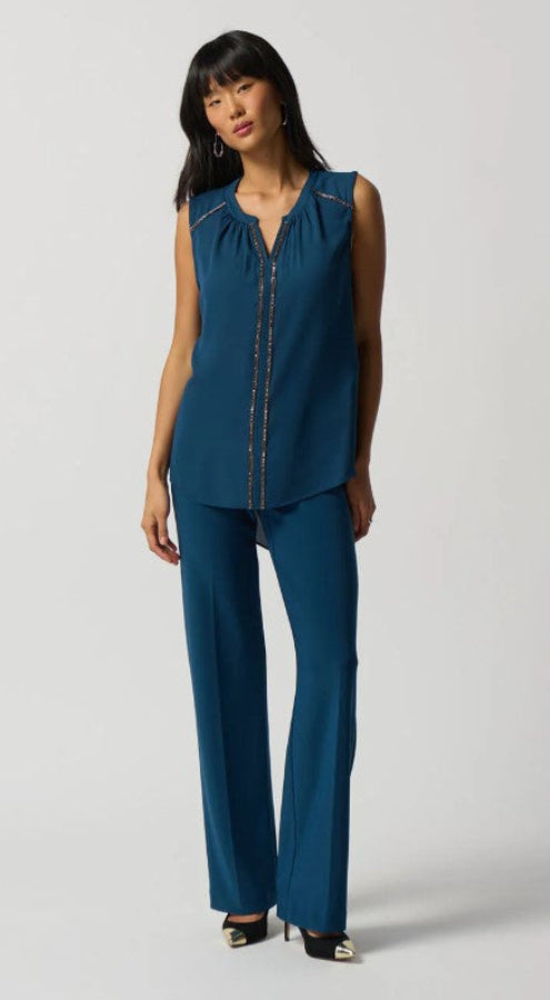 Woman wearing a teal sleeveless top and pants on a white background