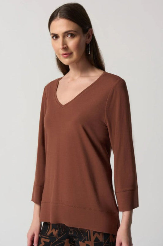 Woman wearing a brown V-neck top against a plain background