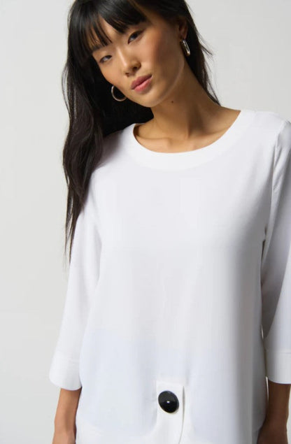 Woman wearing a white blouse with a black button on a plain background