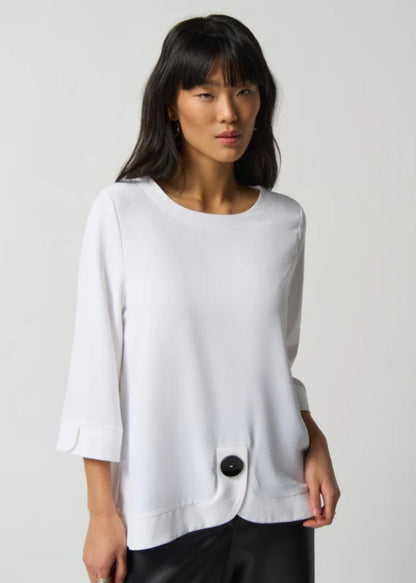 Woman wearing a white blouse with a black button on a plain background