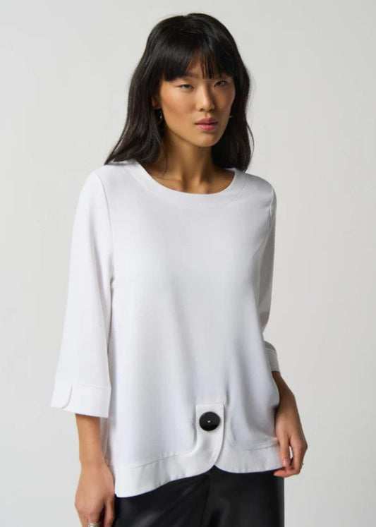 Woman wearing a white blouse with a black button on a plain background