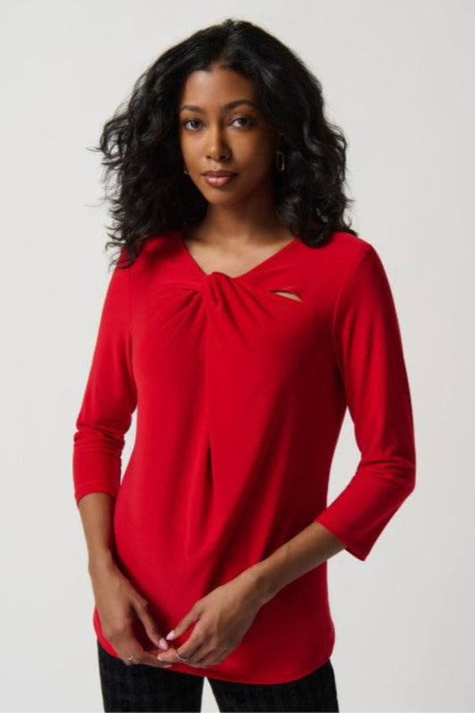 Woman wearing a red long-sleeve top with a knot detail on a plain background