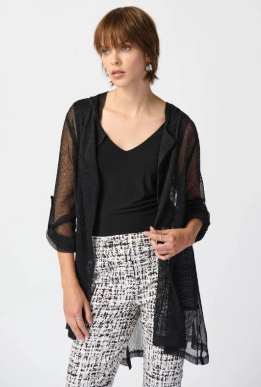 Woman wearing a black sheer jacket over a black top and patterned pants on a white background