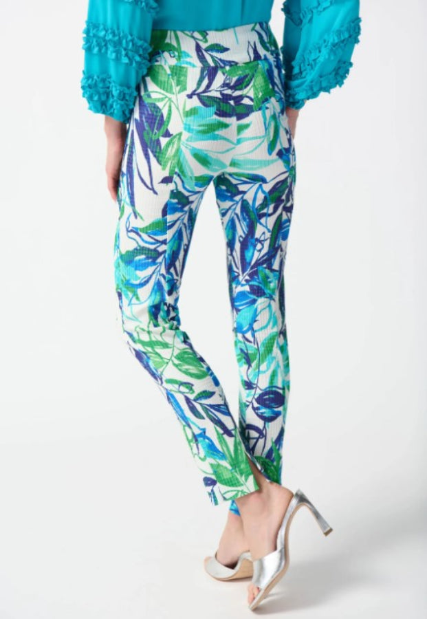 Tropical leaf patterned pants worn with a turquoise top on a white background