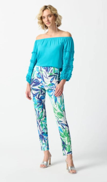 Woman wearing a turquoise off-shoulder top and leaf-patterned pants on a white background