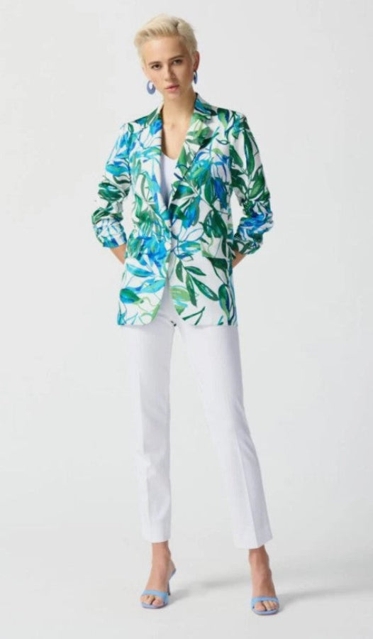 Woman wearing a colorful floral blazer and white pants on a light gray background