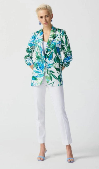 Woman wearing a colorful floral blazer and white pants on a light gray background