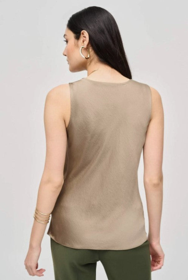 Woman wearing a beige sleeveless top and green pants on a light gray background