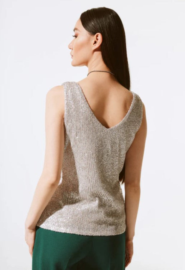 Woman wearing a sleeveless, sparkly top with a plain background