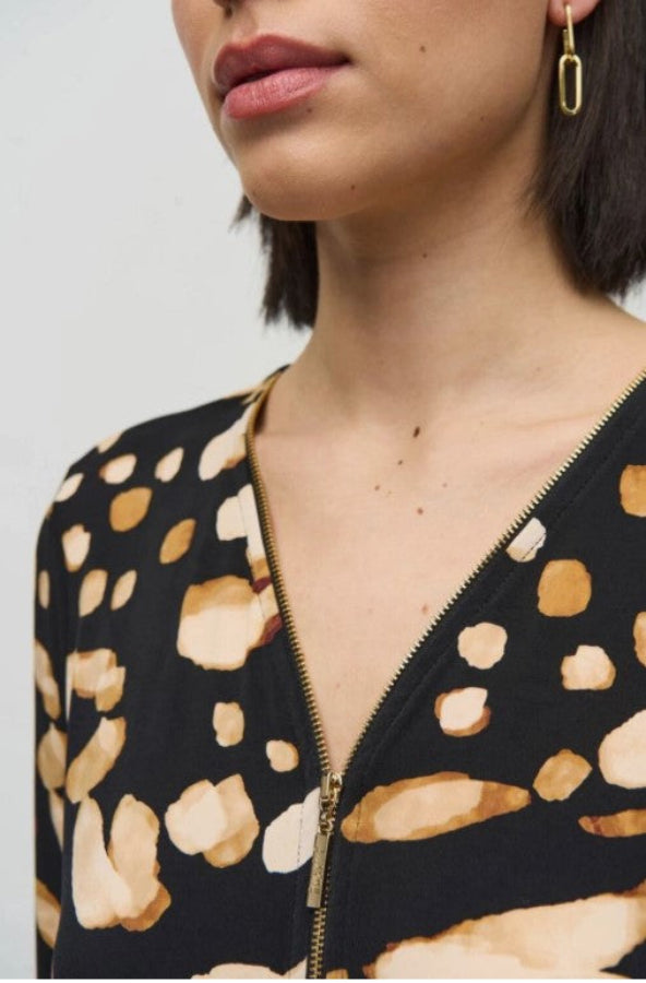 Close-up of a person wearing a black top with a gold zipper and beige pattern.