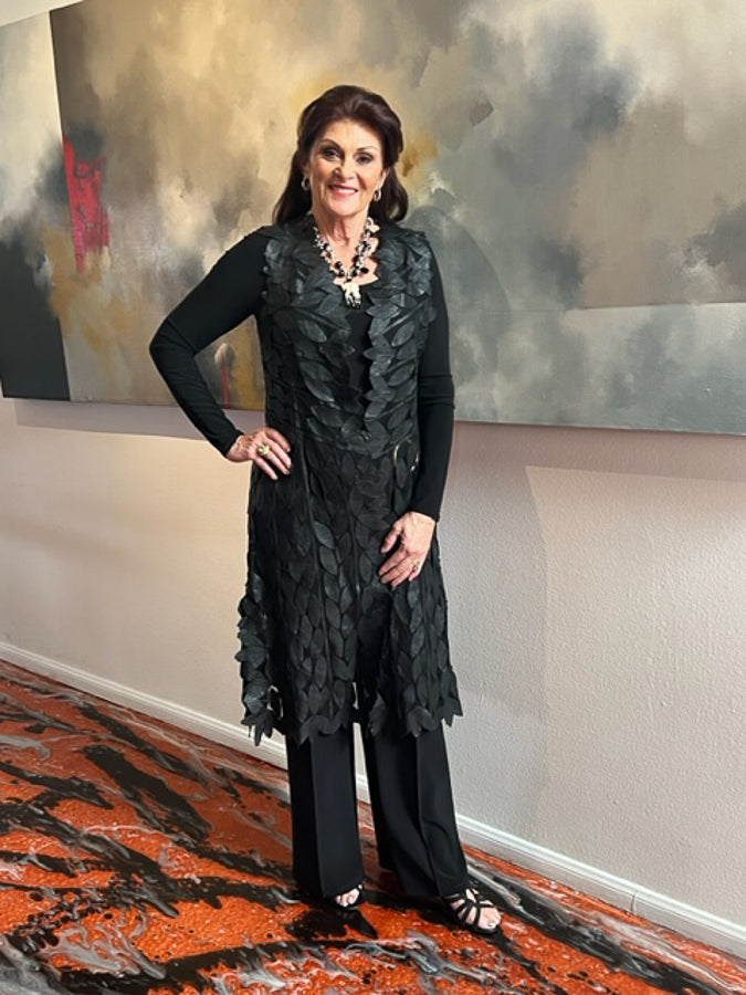 A woman wearing an open front long leather leaf vest in black, with an abstract pattern in bronze and brown tones.